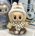 Close-up of a cute tan plush toy doll with a checkered scarf and hat, seated on a printed surface.