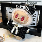 Close-up of a doll dressed in a black and white tweed outfit with a large bow and pearl embellishments. The doll has red heart-shaped eyes and a toothy grin.