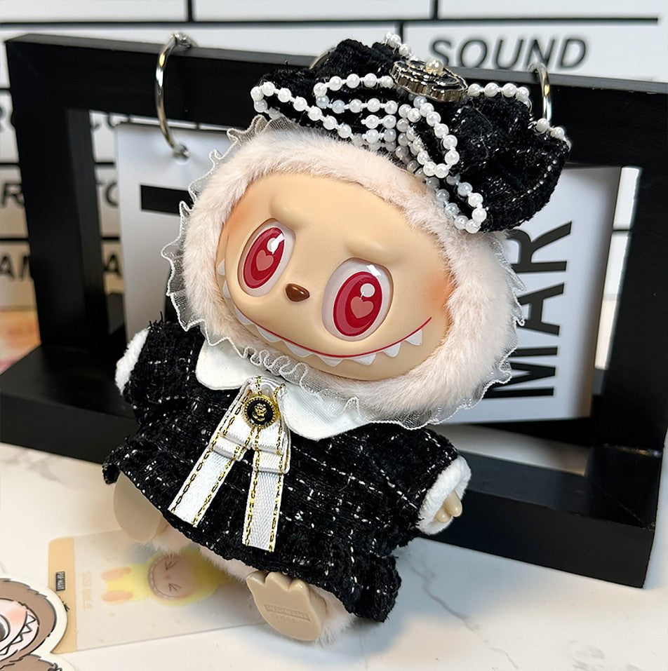 Close-up of a doll dressed in a black and white tweed outfit with a large bow and pearl embellishments. The doll has red heart-shaped eyes and a toothy grin.