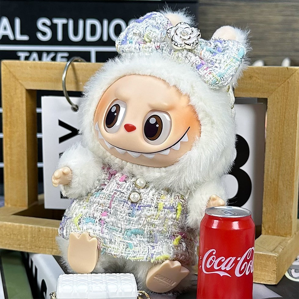 Stuffed toy with a fur-lined hood and tweed jacket, alongside a Coca-Cola can.
