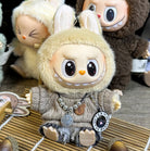 Close-up of a toy doll dressed in a beige sweater and bunny hood, featuring a necklace with charms, sitting on a bamboo mat.
