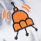 Orange and black embroidered jellysaucer design on silver glittery fabric, by Jellycat, close-up detail showing antennae and signal waves