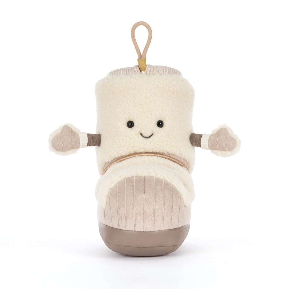 A plush baby boot toy in cream and beige with a smiling face, small fabric hands, and a tan hanging loop at the top, photographed on a clean white background.