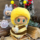 A plush toy dressed as a bee with a yellow hood sits on a small wooden chair.