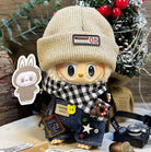 A stylized doll with a tan beanie, a black-and-white checkered scarf, denim overalls with playful patches, standing against a festive backdrop.
