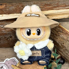 Stuffed plush toy with tan hat, denim overalls, and knit flower.
