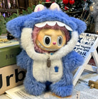 A doll in a blue furry shark costume with a white zipper and hood, resting on a newspaper and books.