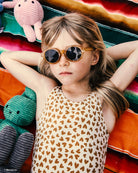 Child wearing sunglasses surrounded by colorful plush toys on a striped blanket
