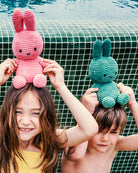 Two children holding pink and green plush toys by a pool.