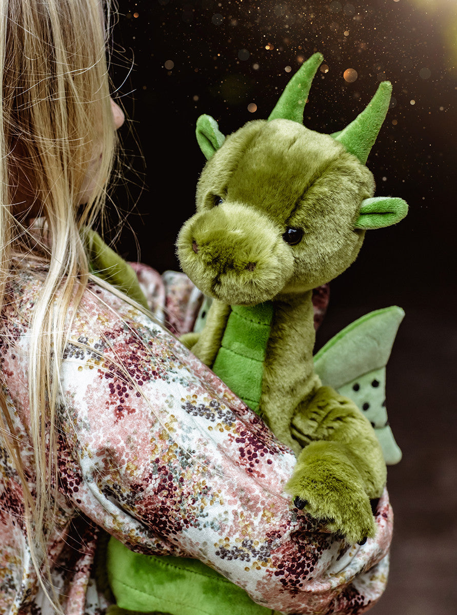 Child holding a green plush dragon toy against a dark background