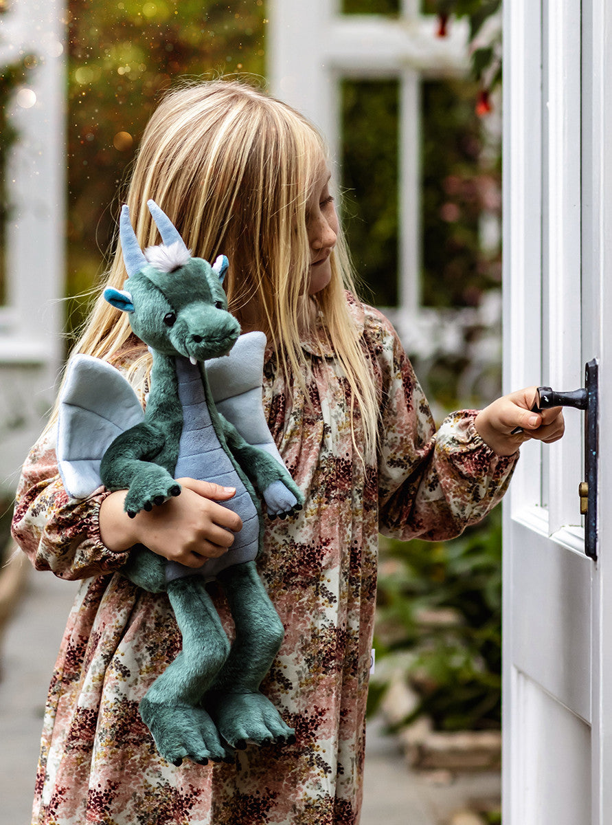 Child holding a plush dragon toy in front of a door