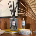 Aromatherapy diffuser, candle, and bottle on a wooden surface with a lamp in the background.