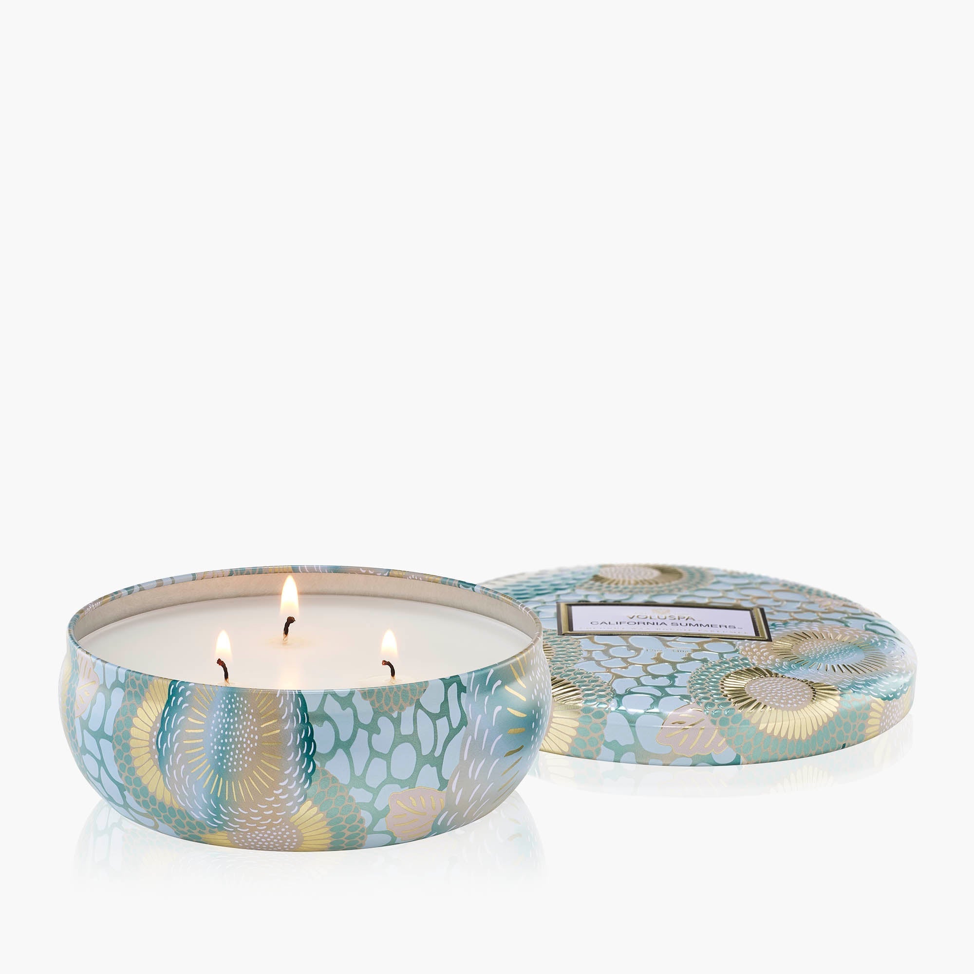 Candle in a decorative tin with a patterned lid on a white background