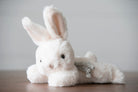 White plush bunny toy with a striped tail on a wooden surface and gray background