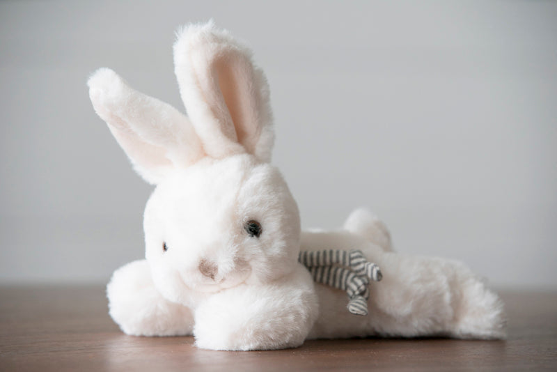 White plush bunny toy with a striped tail on a wooden surface and gray background