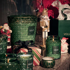 Collection of green candles and decorative items including a nutcracker and Santa Claus figure on a dark surface.