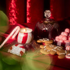 Decorative setup with a lit candle, cookies, and candy on a red surface.