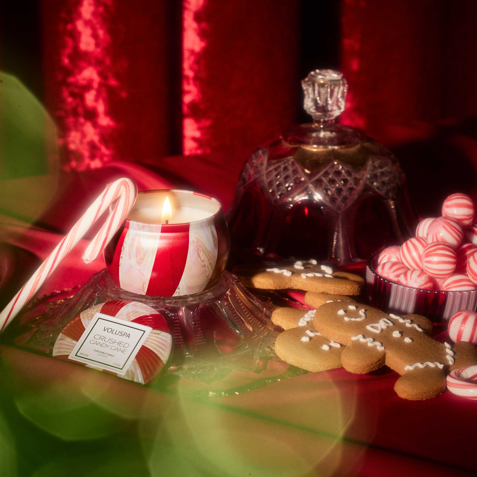 Decorative setup with a lit candle, cookies, and candy on a red surface.