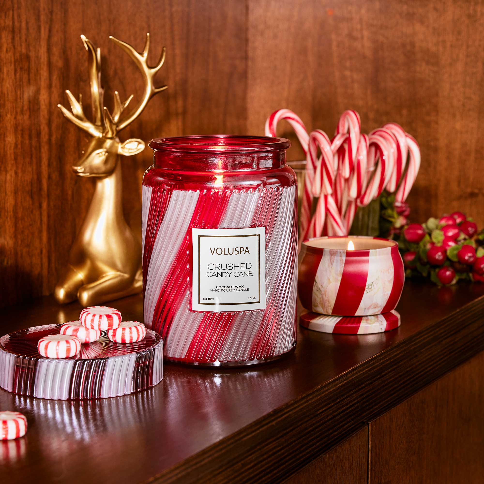 Decorative Voluspa candle with candy cane design on a wooden surface with festive decor.