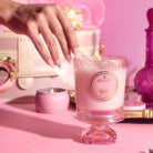 Villosa Pink Cloud candle being lit with a hand on a pink background