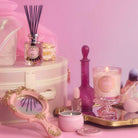 Pink and gold decorative items including candles and a diffuser on a pink background