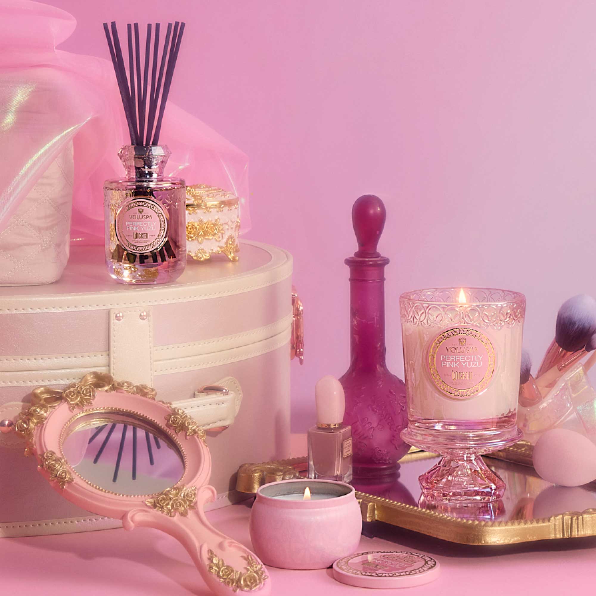 Pink and gold decorative items including candles and a diffuser on a pink background