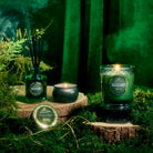 Green-themed candles and diffuser on a wooden surface with a dark green background