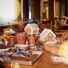 Wooden table with gingerbread houses, baking tools, and a festive background.
