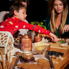 Family gathered around a table with gingerbread house building materials and a candle.