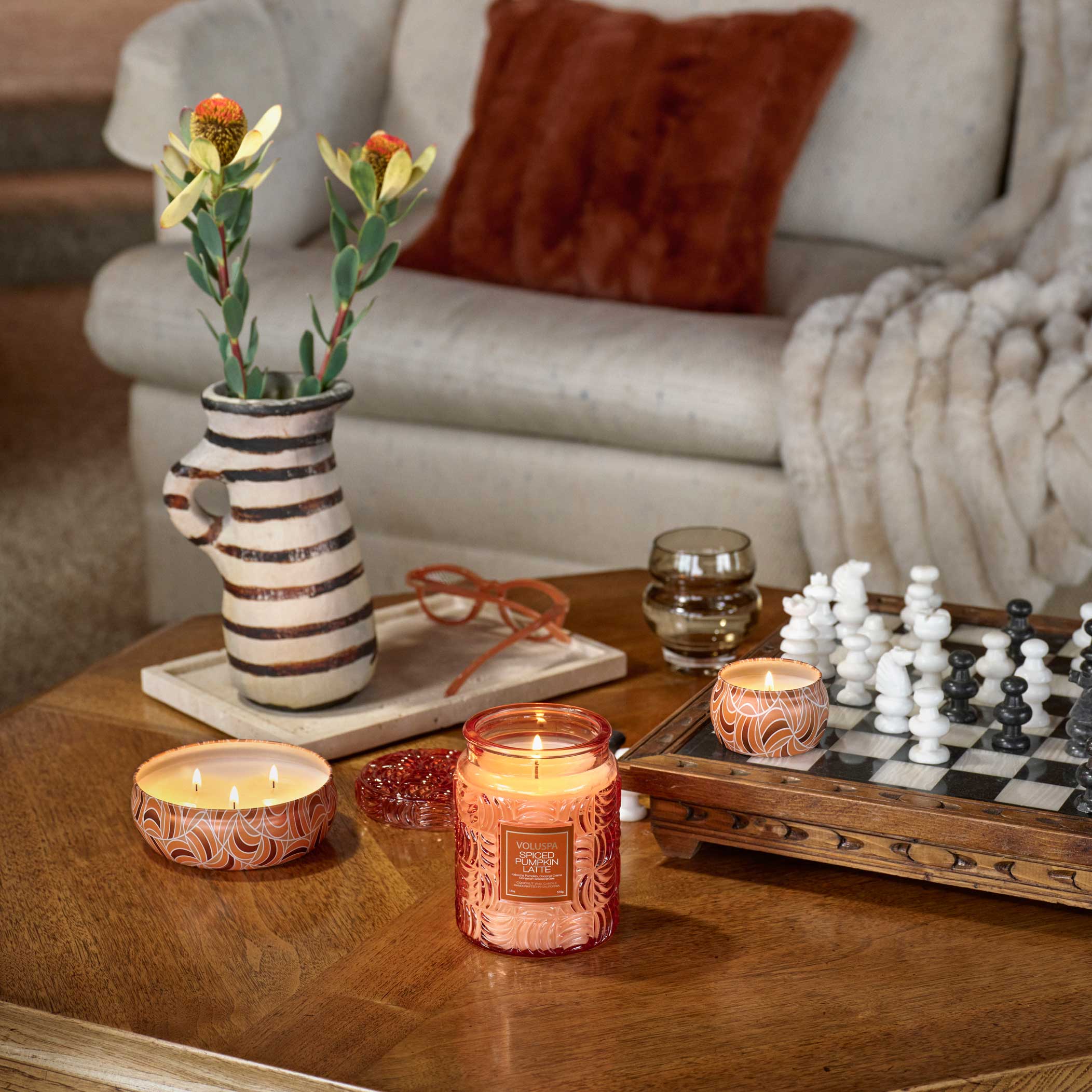 Candlelit living room with candles, a vase, and a chessboard on a coffee table.