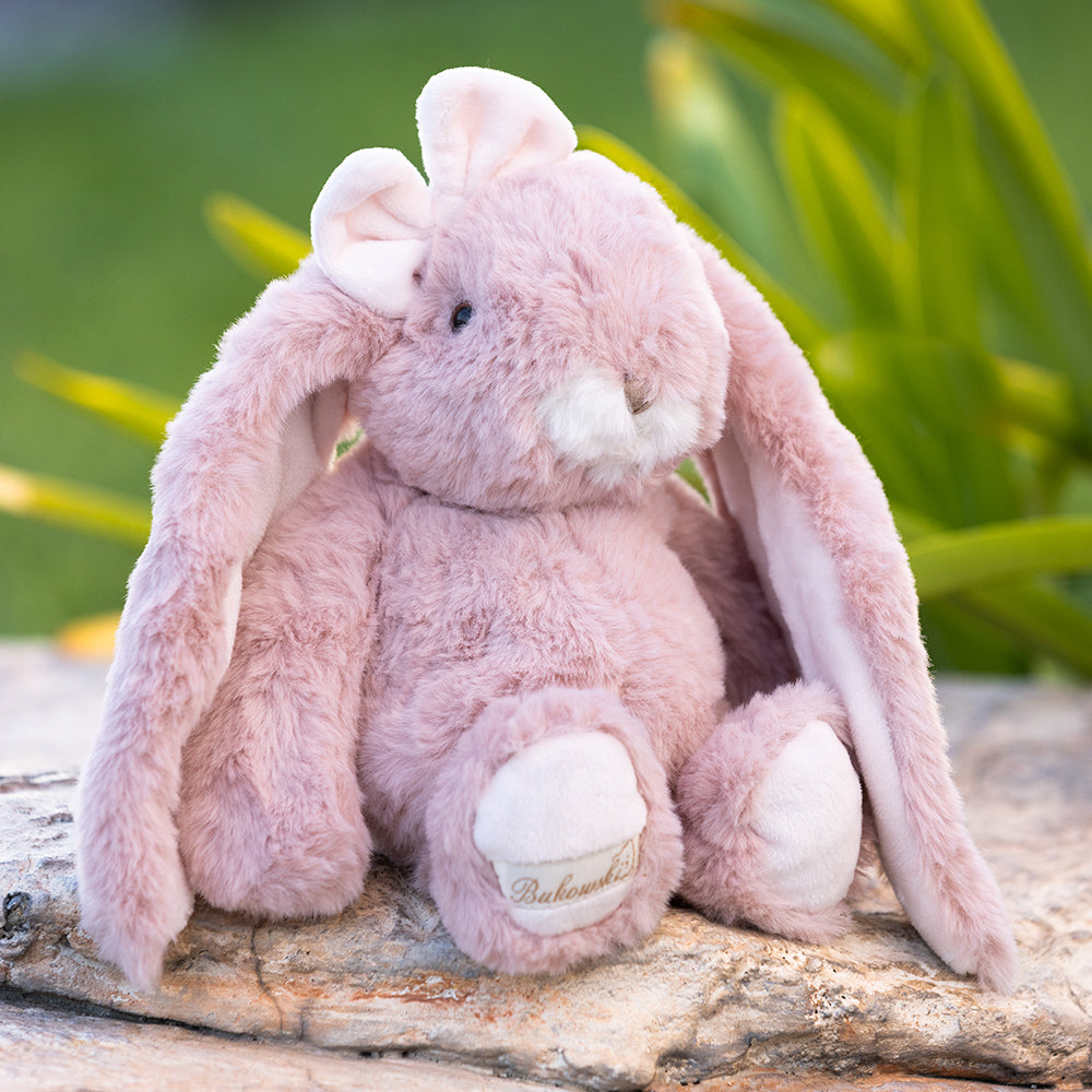 Pink plush bunny sitting on a wooden log with a blurred green background