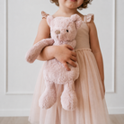 Soft pink plush bear toy by Snuggle Bunnies, held by child in tulle dress, front view, fluffy texture, small black eyes, beige nose