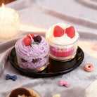 Two small glass desserts with whipped cream and berries on a black plate, surrounded by decorative items.