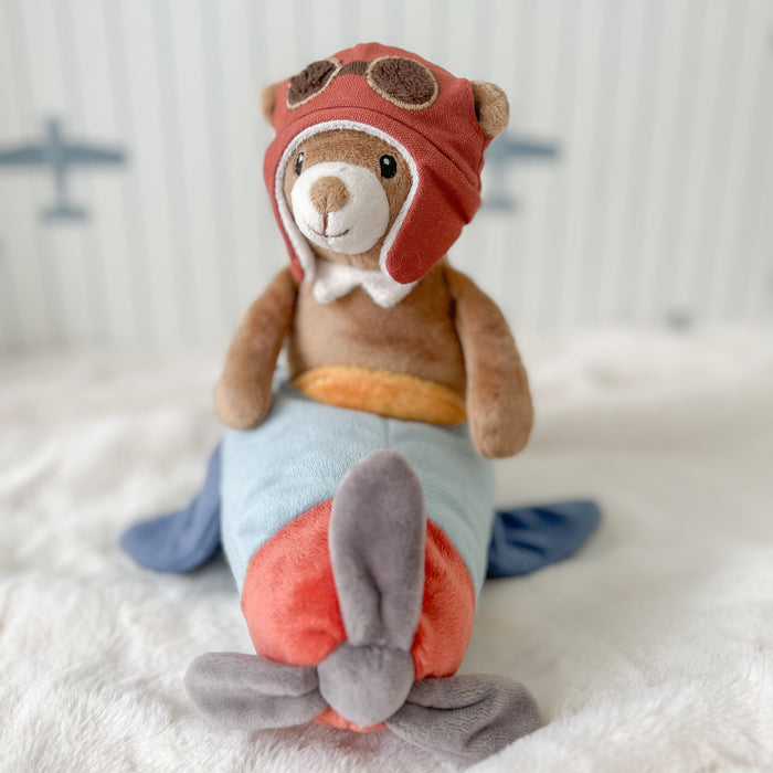 Stuffed toy rabbit in an aviator outfit with a red helmet on a soft surface.