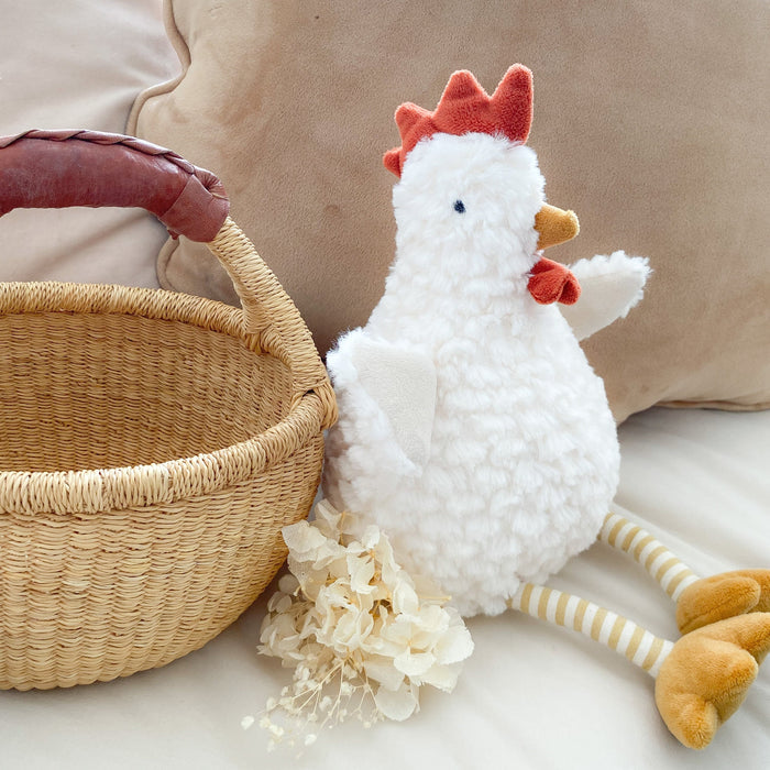White plush chicken toy with red crest and yellow legs next to a woven basket on a beige couch.