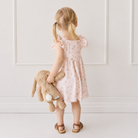 Soft tan plush bunny toy with white tail, held by child in floral dress, back view lifestyle shot