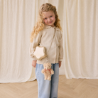 Plush tan bear keychain with red bow by Snuggle Bunnies, attached to star-shaped bag, worn by child in cream cardigan and jeans, front view.
