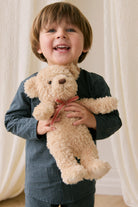 Child holding a teddy bear with a red bow in front of white curtains