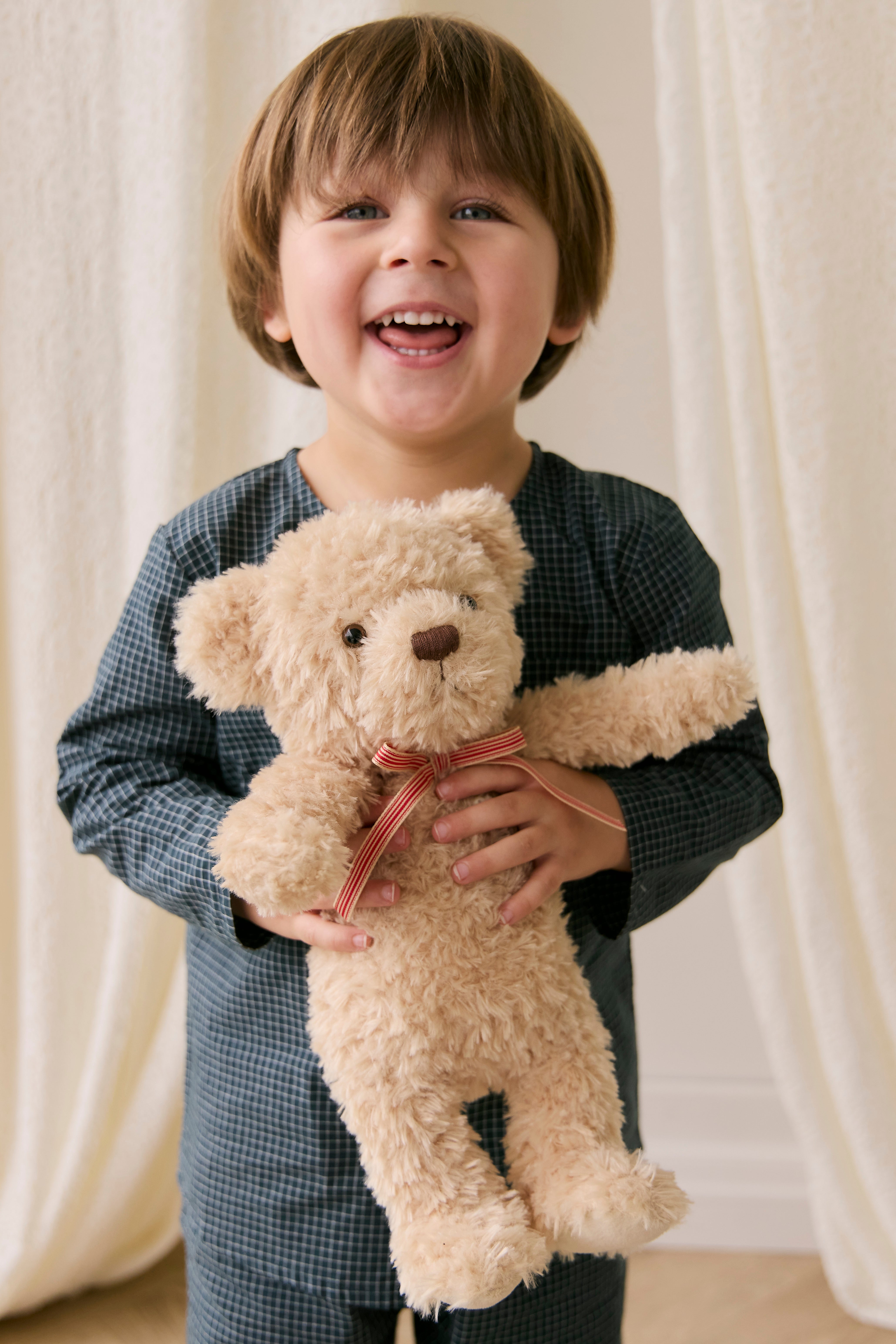 Child holding a teddy bear in front of white curtains