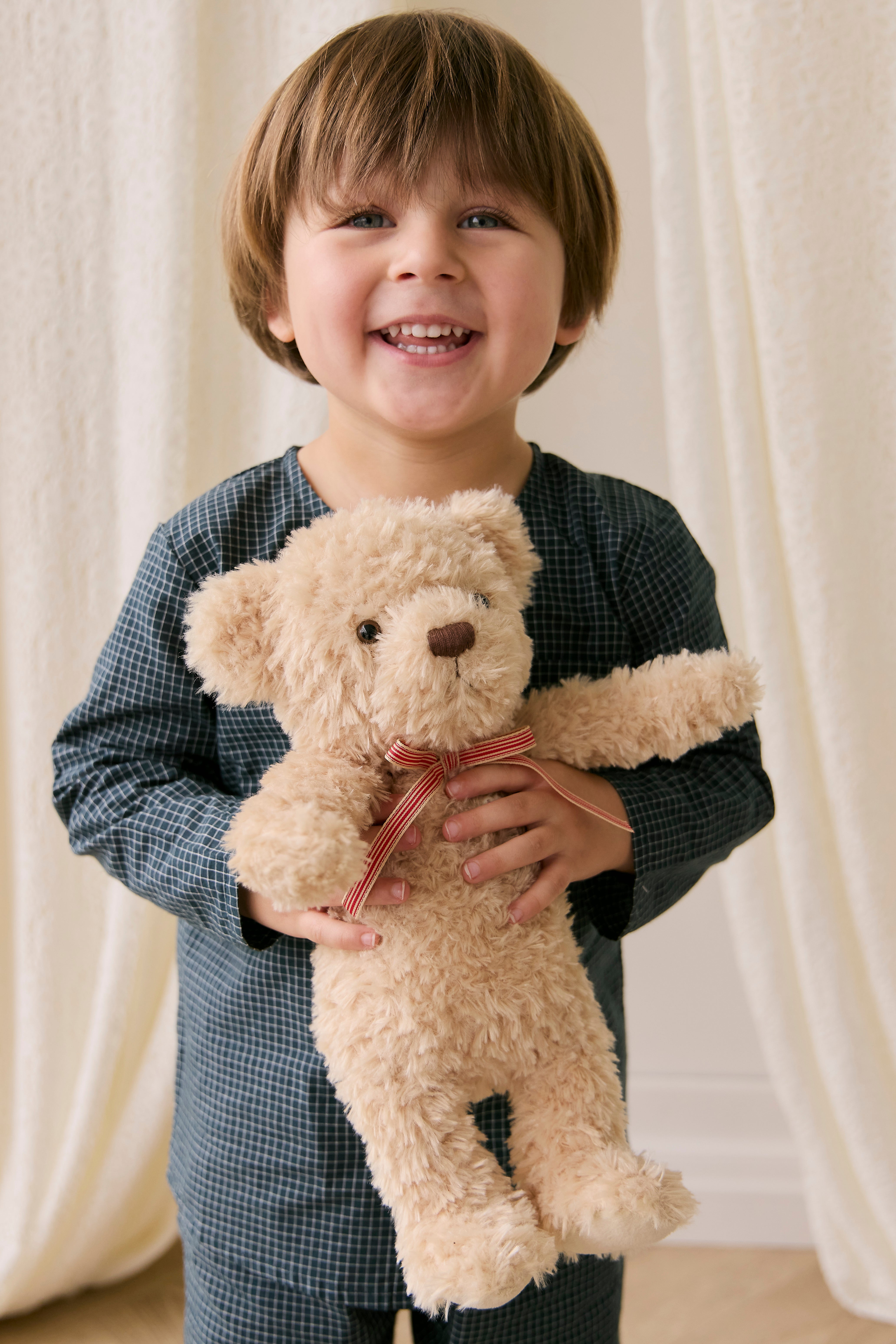 Child holding a teddy bear in front of white curtains