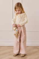 Young girl in a light-colored outfit holding a teddy bear in a minimalistic setting