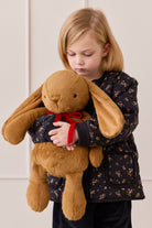 Child holding a large brown plush bunny with a red bow tie against a white background
