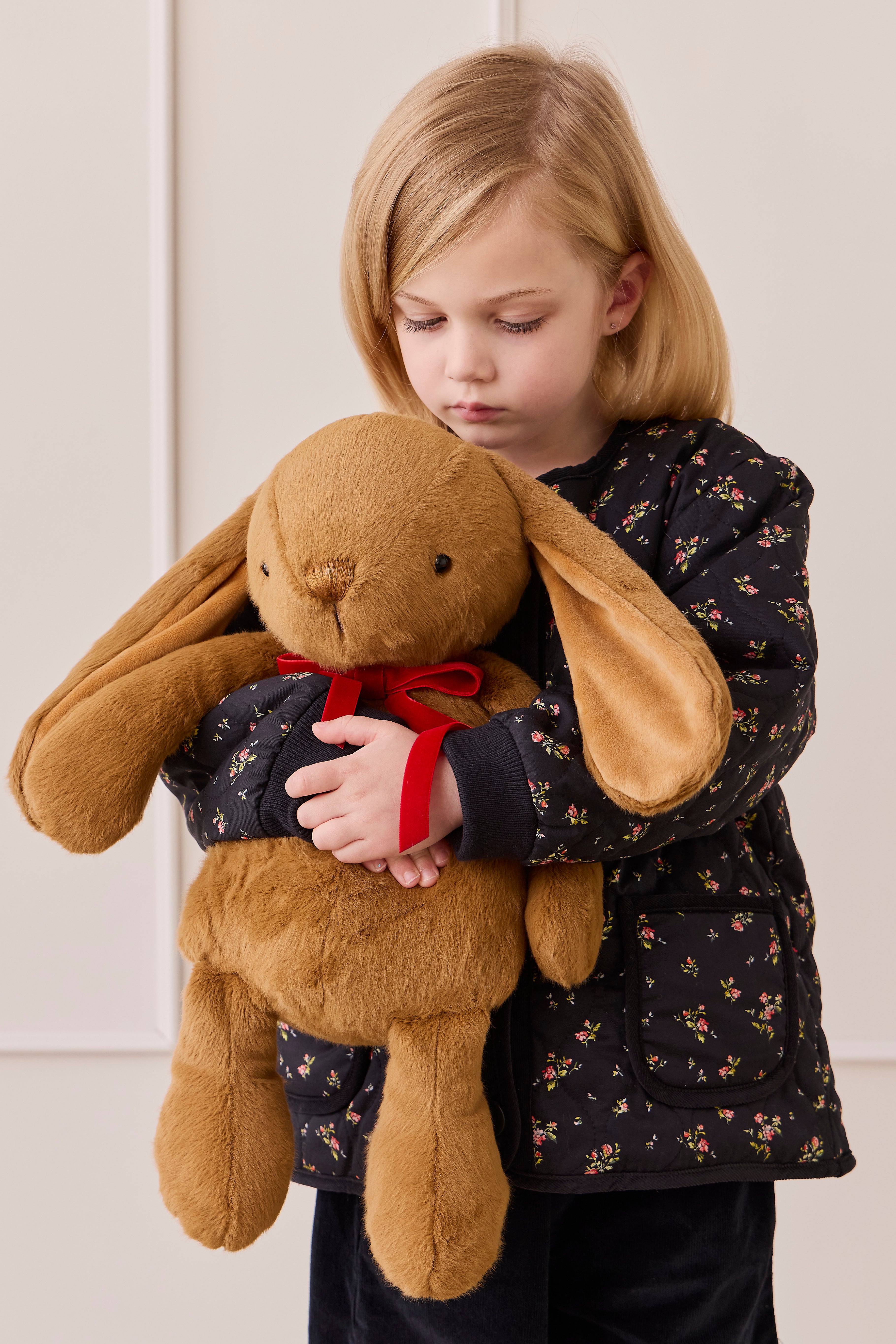 Child holding a large brown plush bunny with a red bow tie against a white background