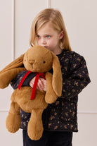 Child holding a large brown teddy bear with a red bow against a light background