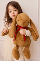 Young girl holding a large brown plush bunny with a red bow.