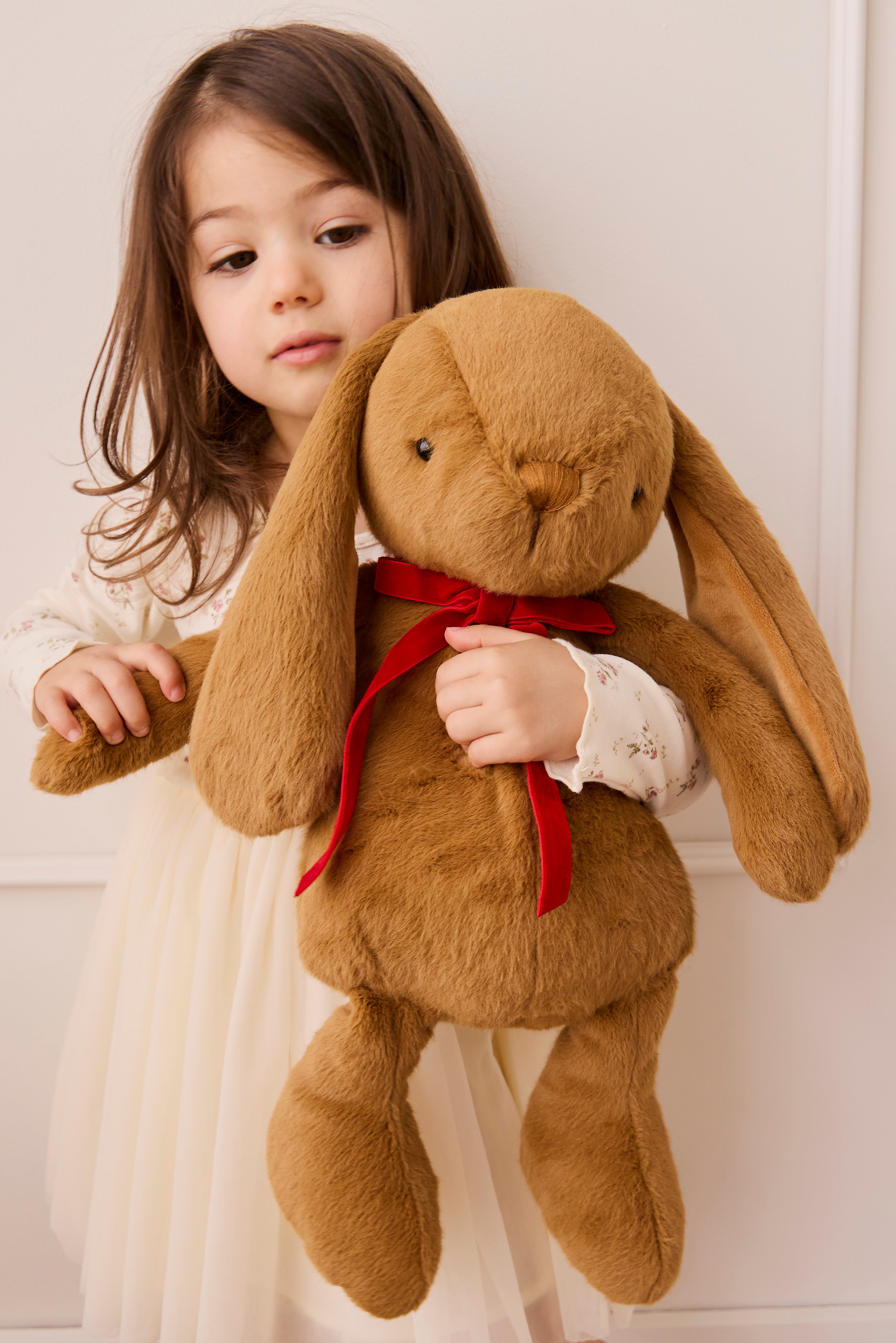 Young girl holding a large brown plush bunny with a red bow.