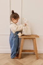 Child playing with a plush toy on a wooden stool against a white wall.