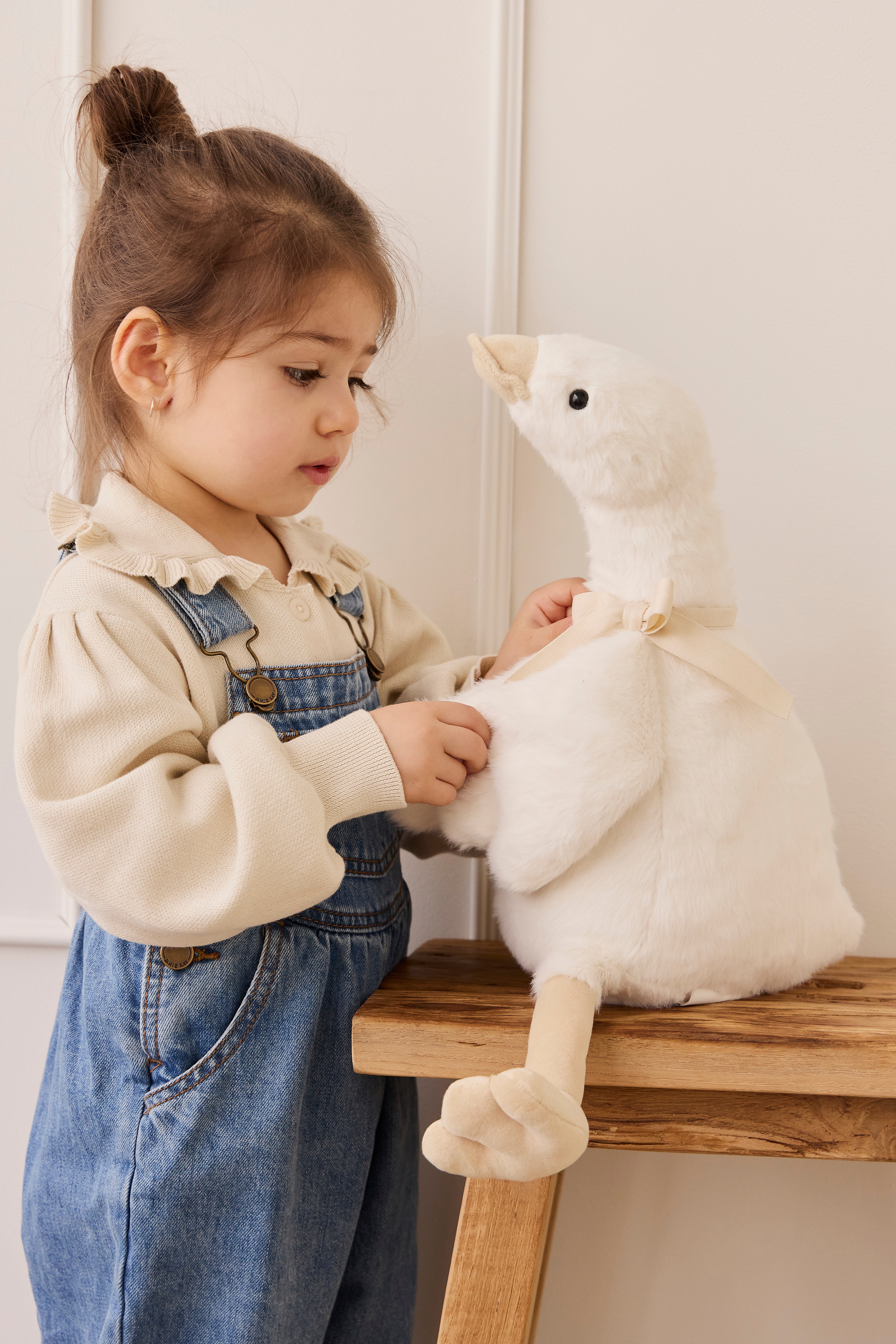 Child playing with a plush toy on a wooden stool against a white wall.
