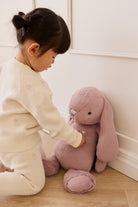 Child playing with a plush toy in a room with white walls and wooden floor.