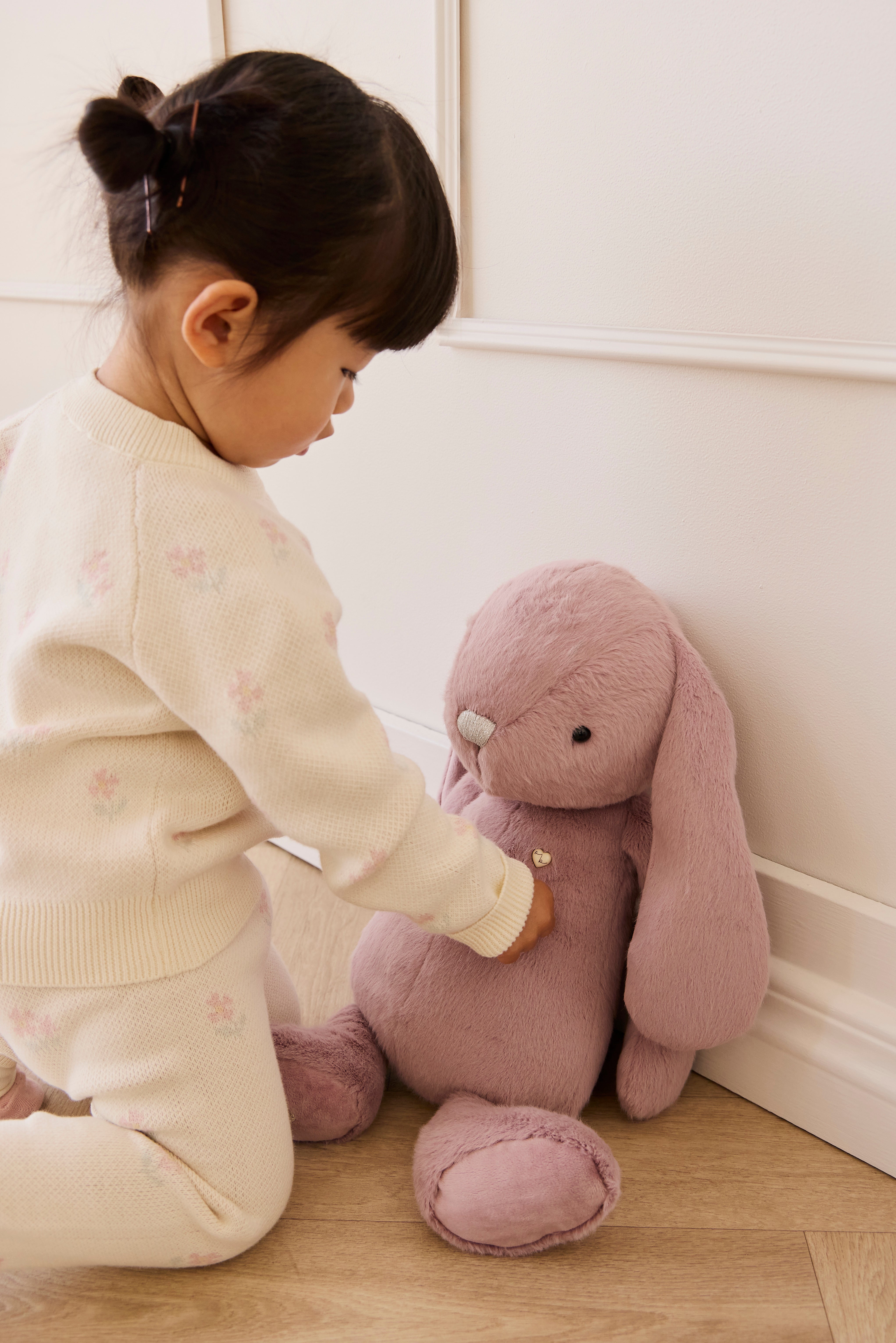 Child playing with a plush toy in a room with white walls and wooden floor.